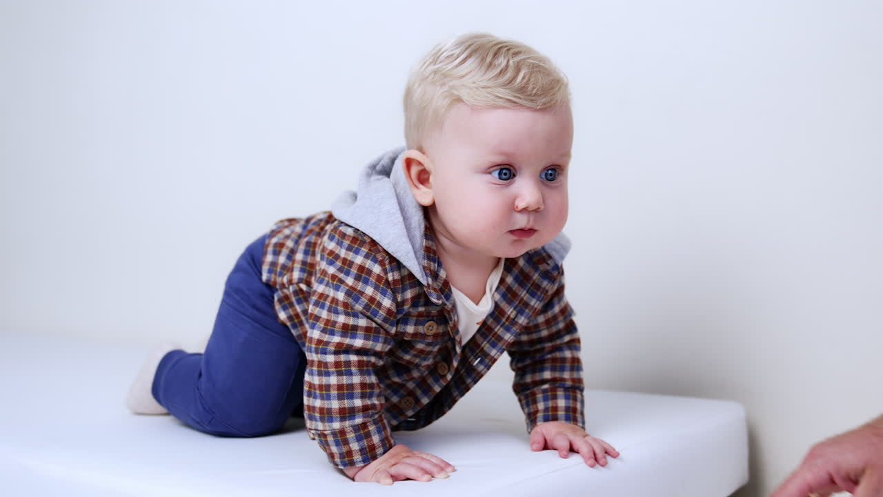 Cute blond baby boy drops on all four. Dad holds his hand for the son. Close up. White backdrop.
