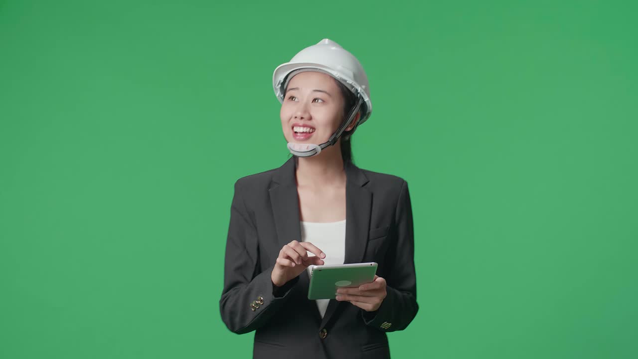 Smiling Asian Female Engineer Looking Around And Shaking Her Head While Using Tablet And Walking In The Green Screen Studio