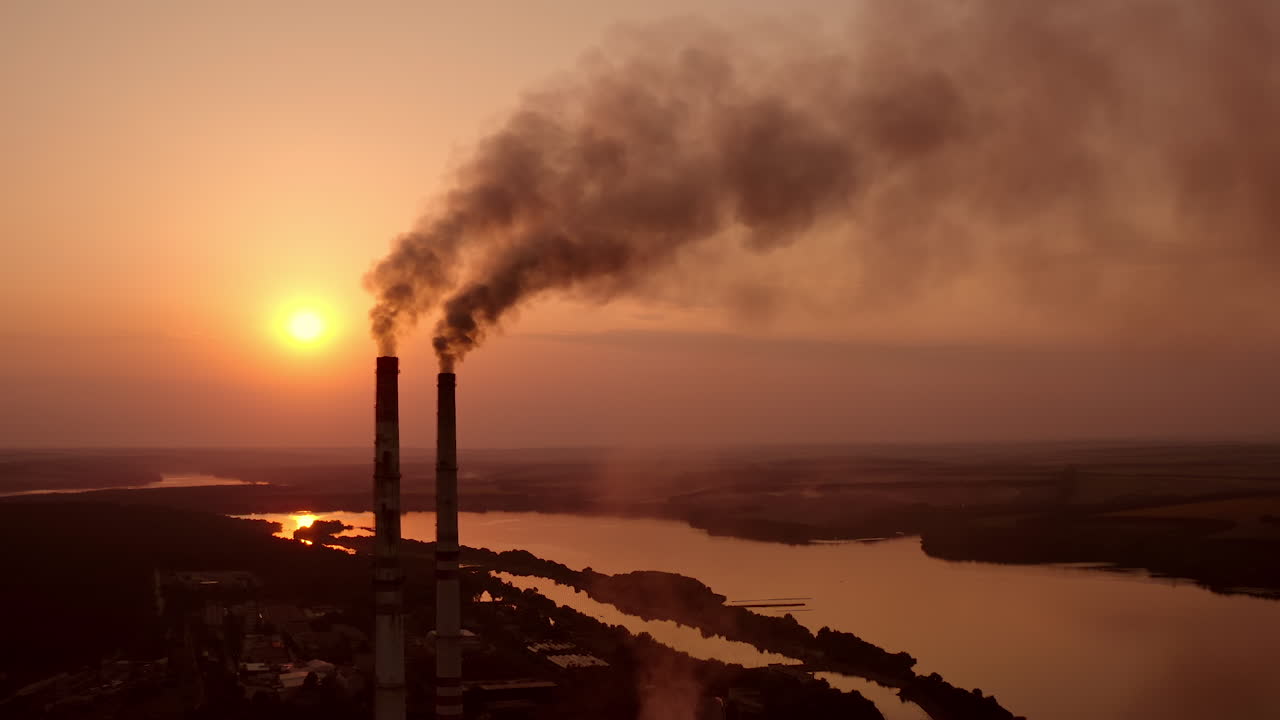 Dangerous fumes from industry pollute the air. Harmful factory with smoking pipes near river at sunset. Global warming. Environmental pollution.