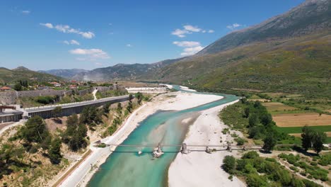 Old-bridge-over-Vjosa-river-flowing-alongside-road-on-beautiful-landscape-in-Albania