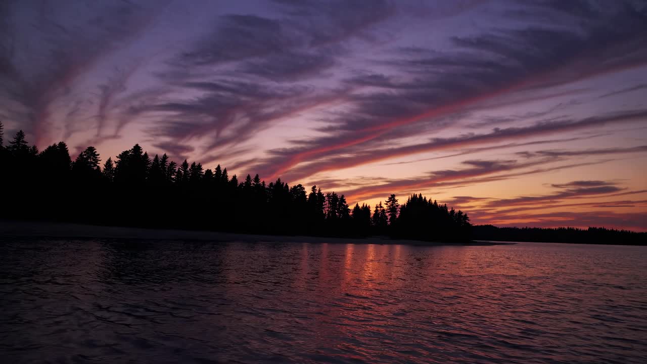 Stunning wide-angle video capture of a serene sunset over a lake, with silhouetted trees