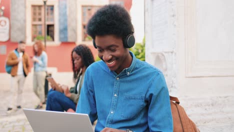 African-american-man-using-a-laptop-while-sitting-on-the-ground-in-the-street