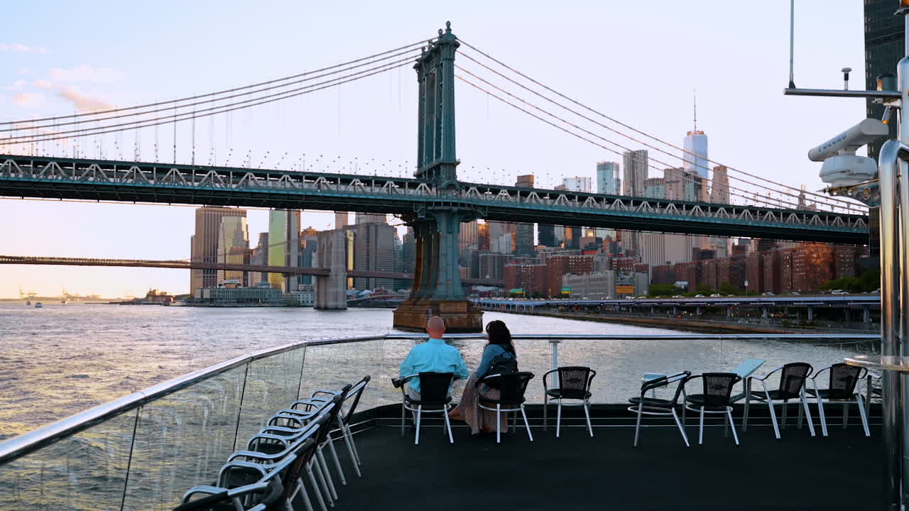 New York, USA, 1 aprile 2026: Posti a sedere sul ponte scoperto di fronte allo skyline del Ponte di Manhattan. Ponte di barca scoperto con sedie di fronte al Ponte di Manhattan, allo skyline, al fiume, luce serale