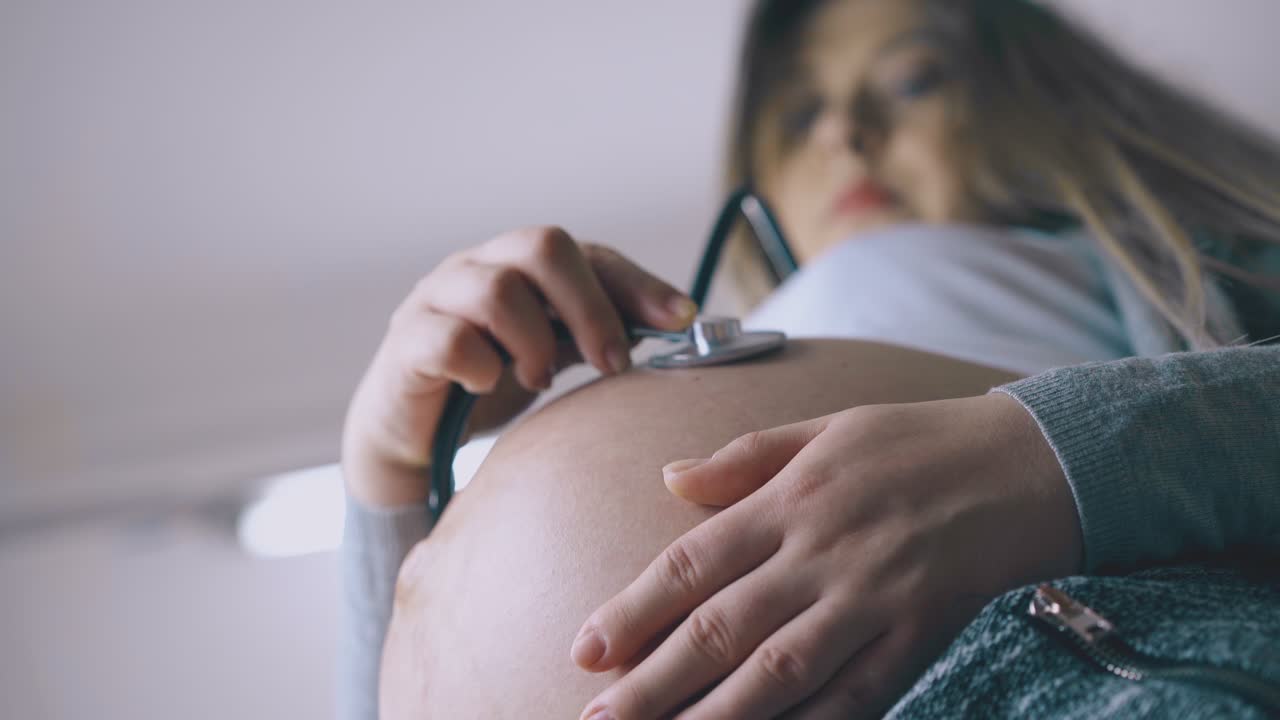 una donna incinta con la pancia ascolta il battito cardiaco del bambino da vicino