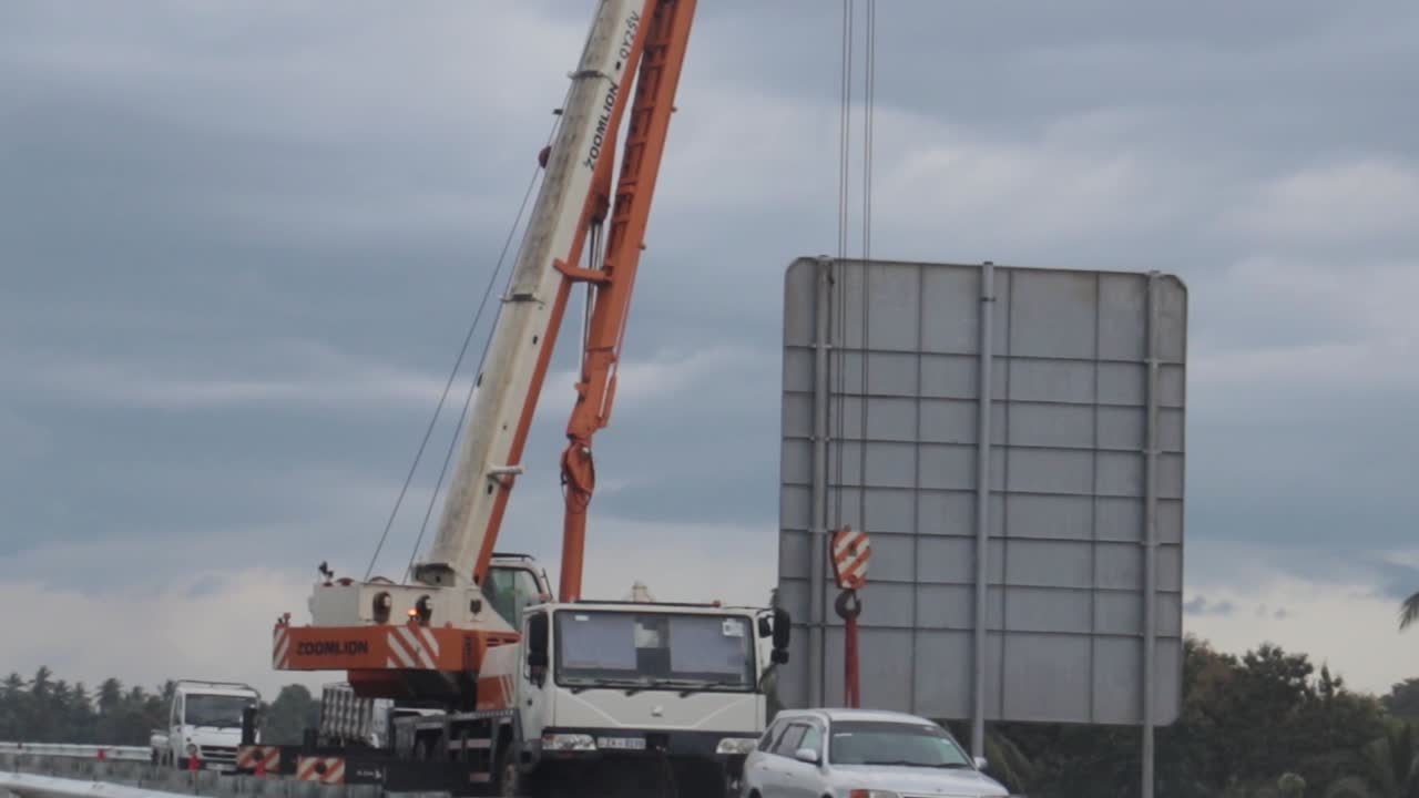 Expressway construction site passing by, billboard placement using a crane is underway.