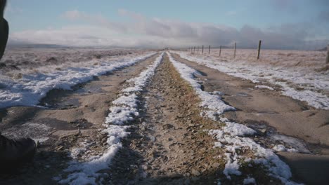 two people walking past the camera, hiking away along a long, snowy, frozen trail through open moorland on a beautiful winter day