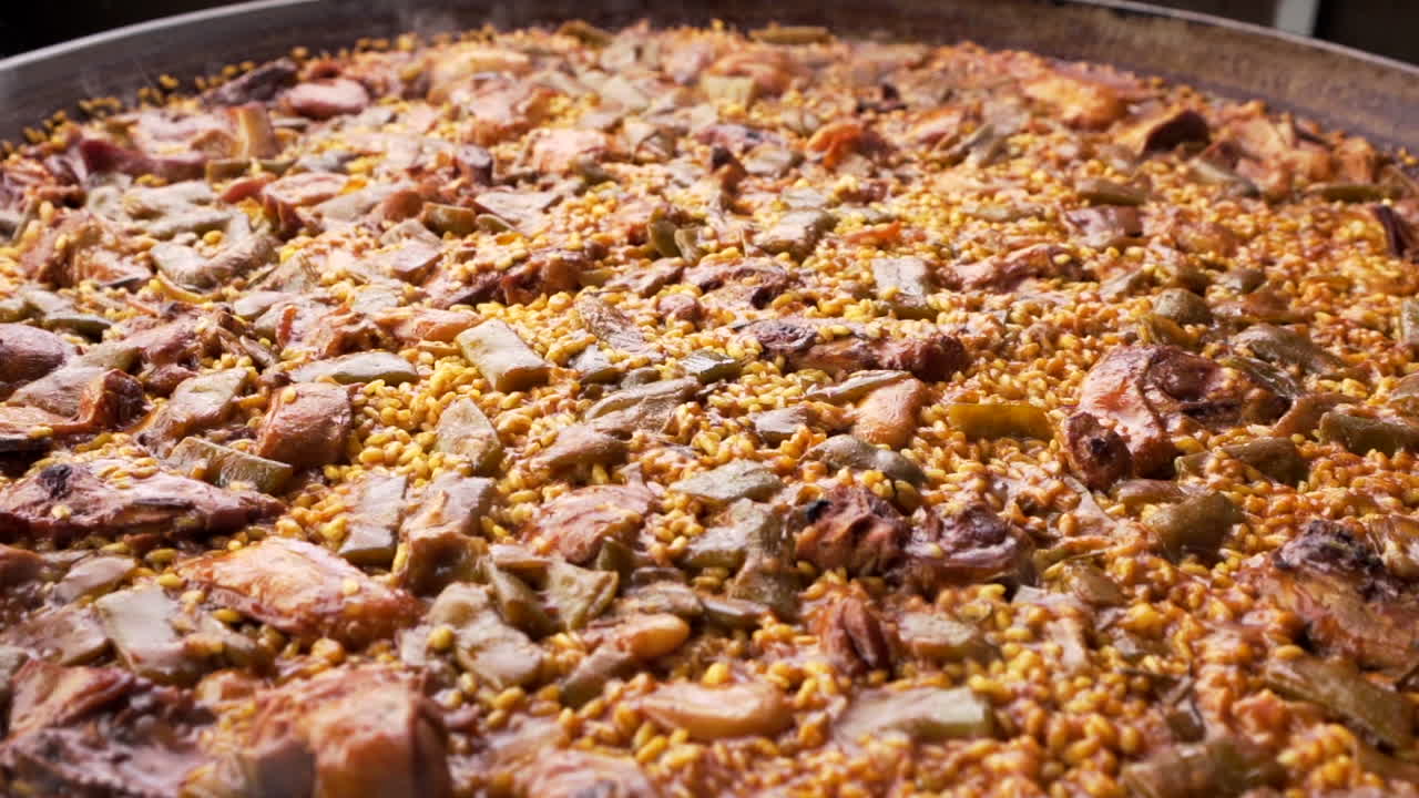 Paella Valenciana i en stor panne, laget med ris, kylling og grønnsaker under tilberedning.