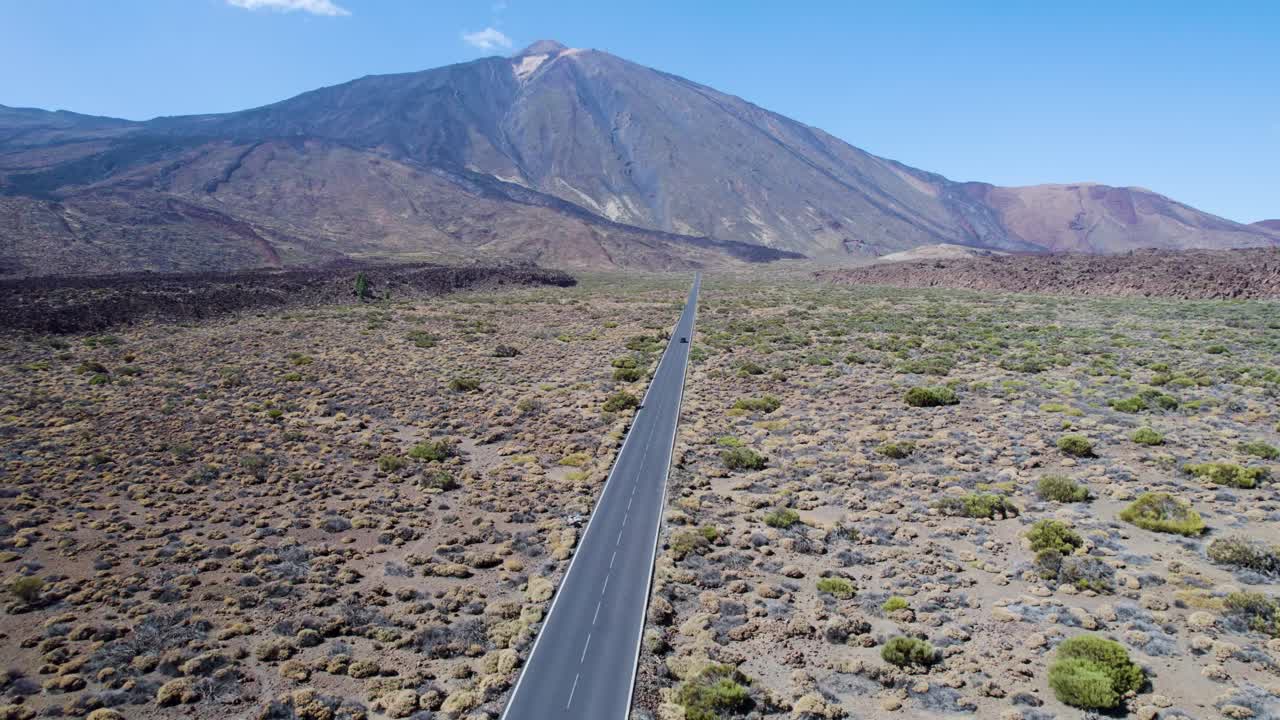 Strada dritta che conduce verso il vulcano Teide, con un'auto che attraversa il terreno vulcanico a Tenerife, Spagna, adatta per riprese di viaggio e di destinazione