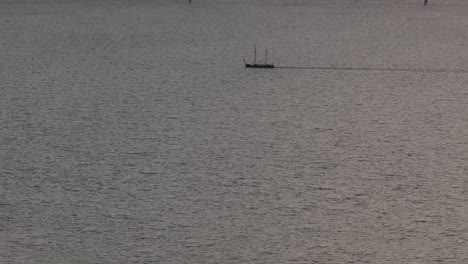 Aerial-view-of-sailing-vessel-with-In-the-background-big-windfarm-with-turbines-at-sunset,-IJsselmeer,-Netherlands