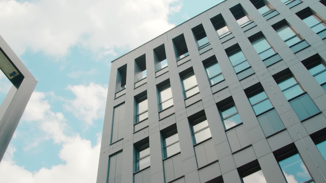 Part of the facade of a modern business center building is a bottom-up view. The sky reflected in the windows of the building.
