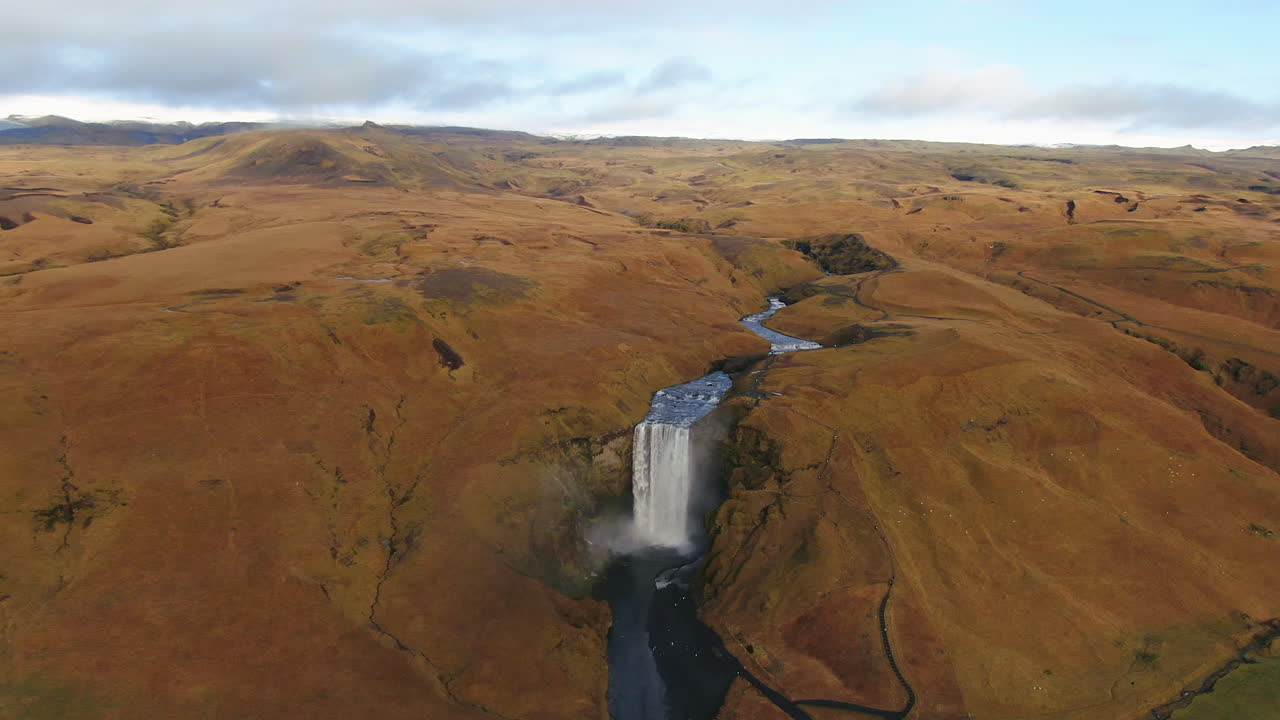 avión no tripulado cinematográfico cascada de skogafoss islandia pan movimiento hacia atrás arriba con pájaros, arco iris y luz del sol de la tarde