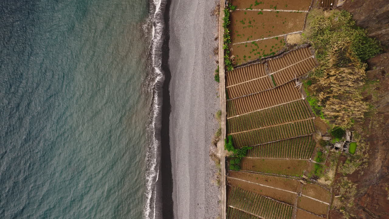 Veduta aerea delle onde dell'oceano su una spiaggia di ciottoli e campi agricoli.