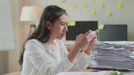 사무실에서 문서 작업을 한 후 스마트폰에서 게임을 잃은 아시아 여성이 화를 내고 있는 클로즈업