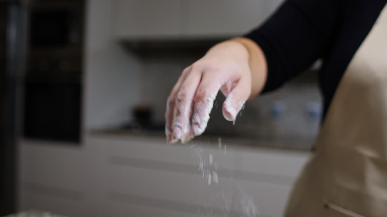 Woman’s hand dusting flour liberally in slow motion close-up.