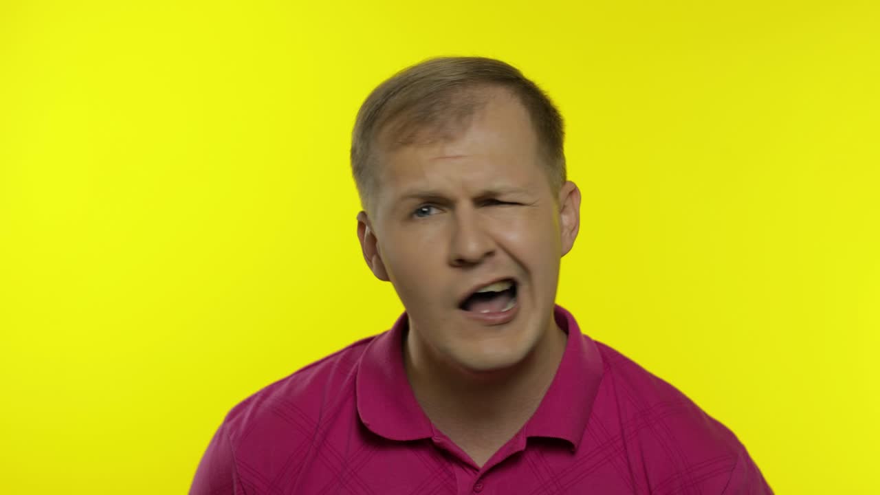 Portrait of young caucasian man posing in pink t-shirt. Dissatisfied, picky guy looking to camera