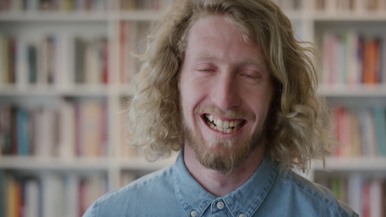 retrato feliz joven hombre rubio estudiante riendo disfrutando de una educación exitosa estilo de vida independiente hombre caucásico en la biblioteca librería de fondo cámara lenta