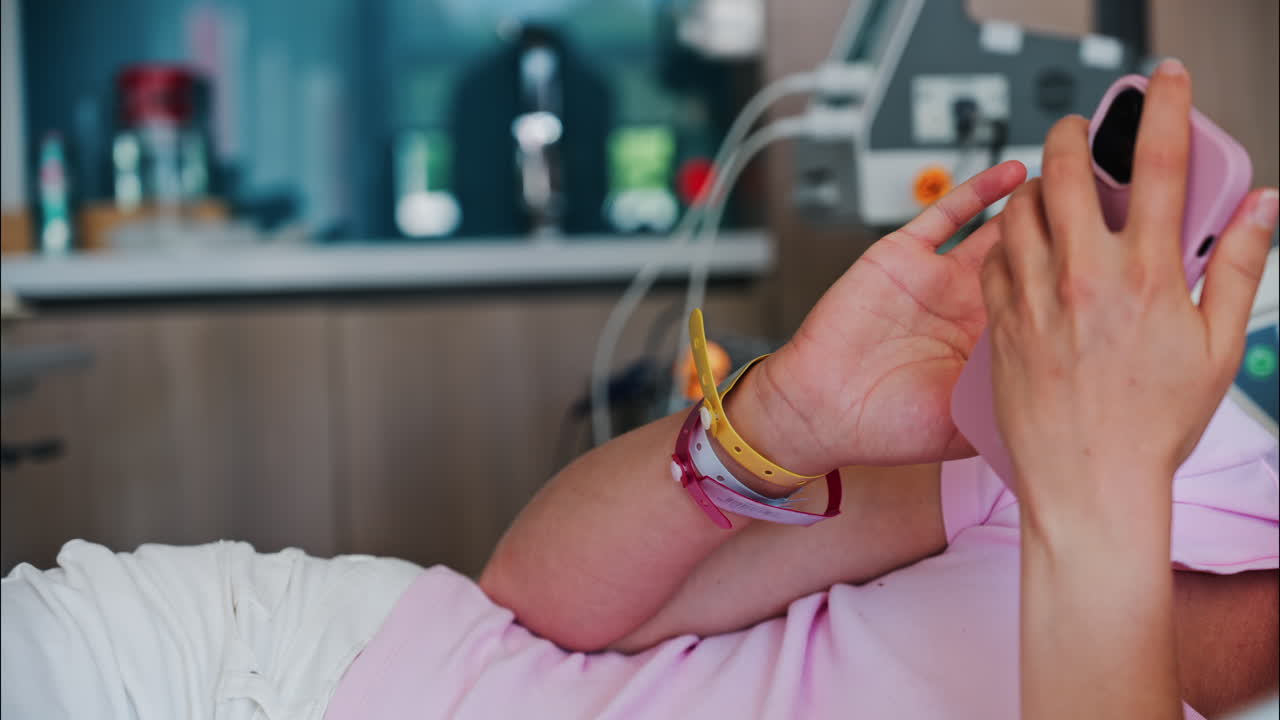 Pregnant woman scrolling on her phone while lying in a hospital bed at the doctor's office