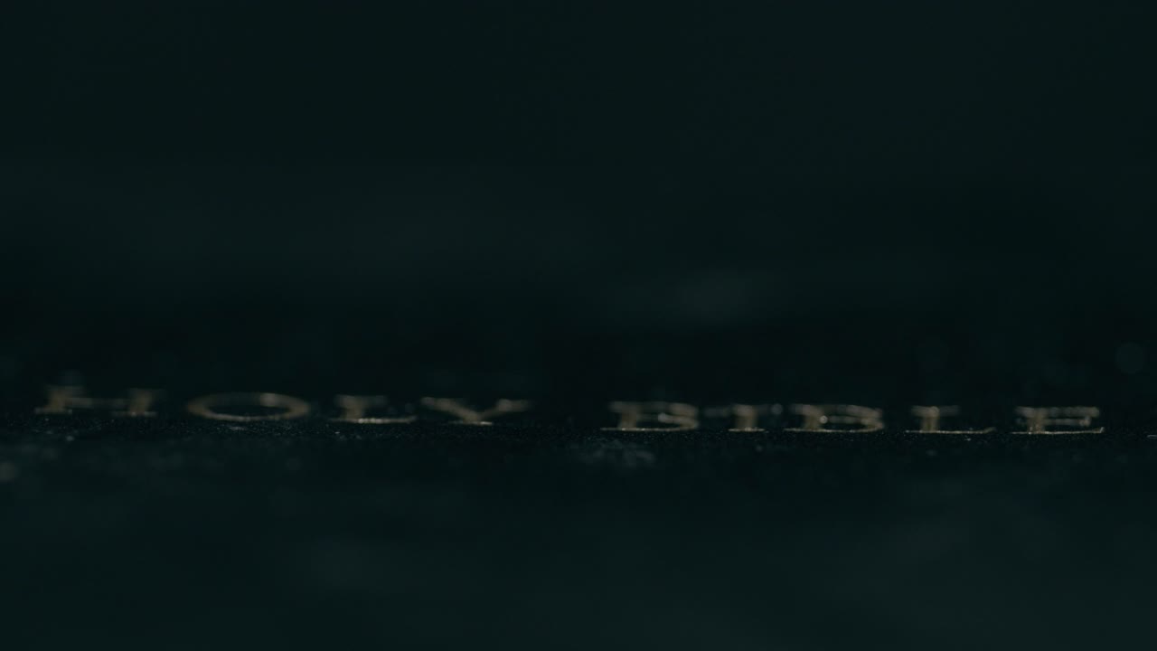 A detailed view of a Holy Bible cover, illuminated by dramatic, soft light against a dark background, creating an intimate, reverent atmosphere in this close-up shot