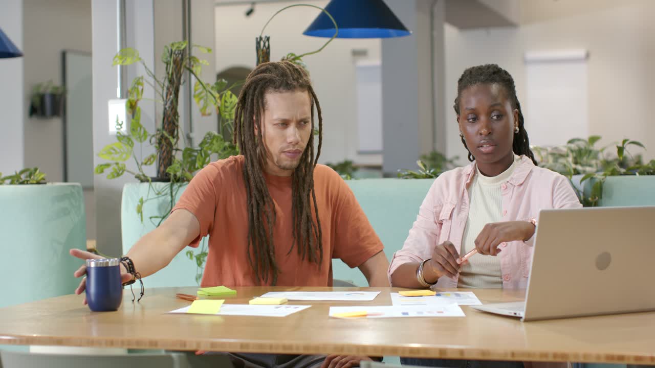 African American team planning at office after man sipping blue mug and arranging notes with laptop