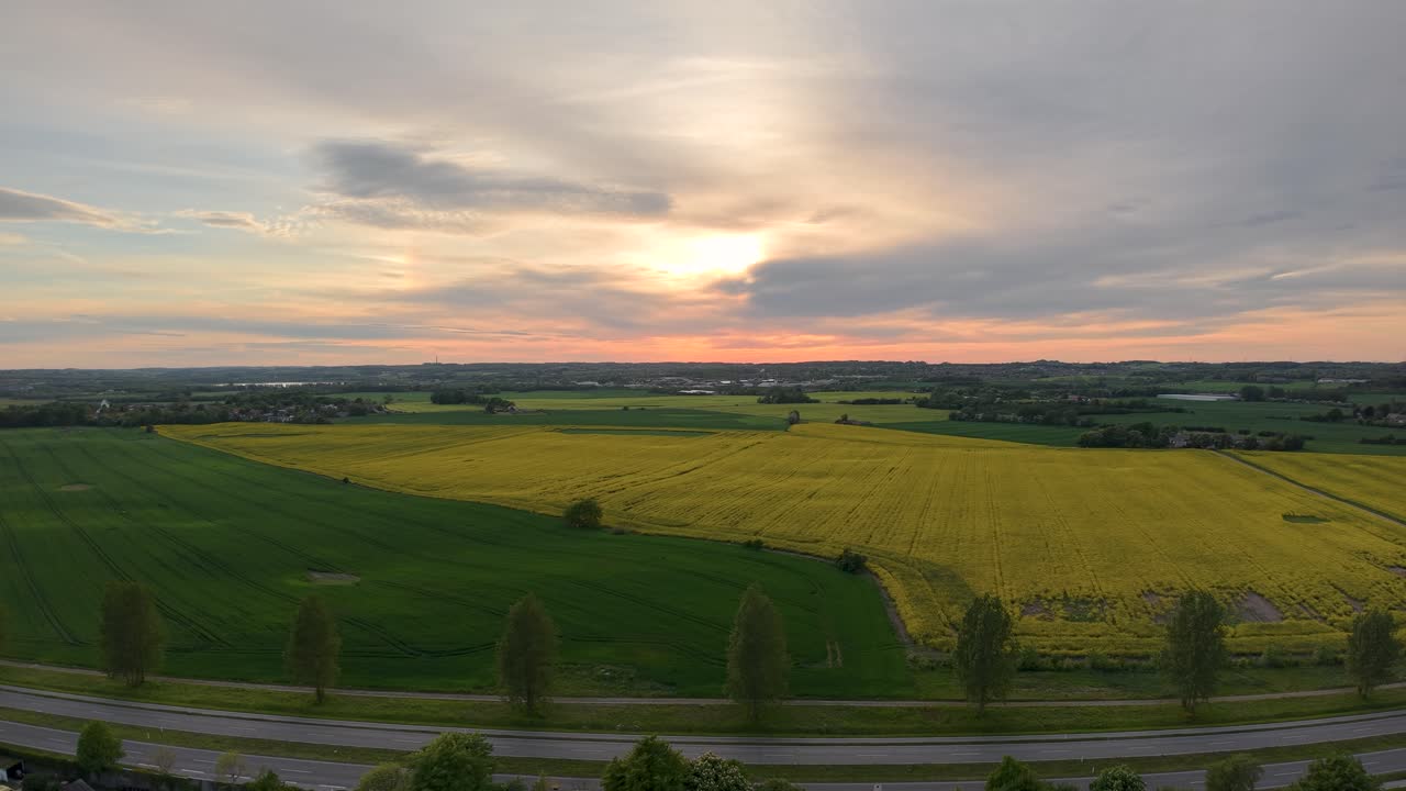 Drone footage of expansive farmland with fields of green and yellow under a dramatic sunset sky