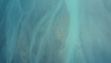 top down drone shot of beautiful blue water of lake tekapo transitioning into braided river, new zealand, south island