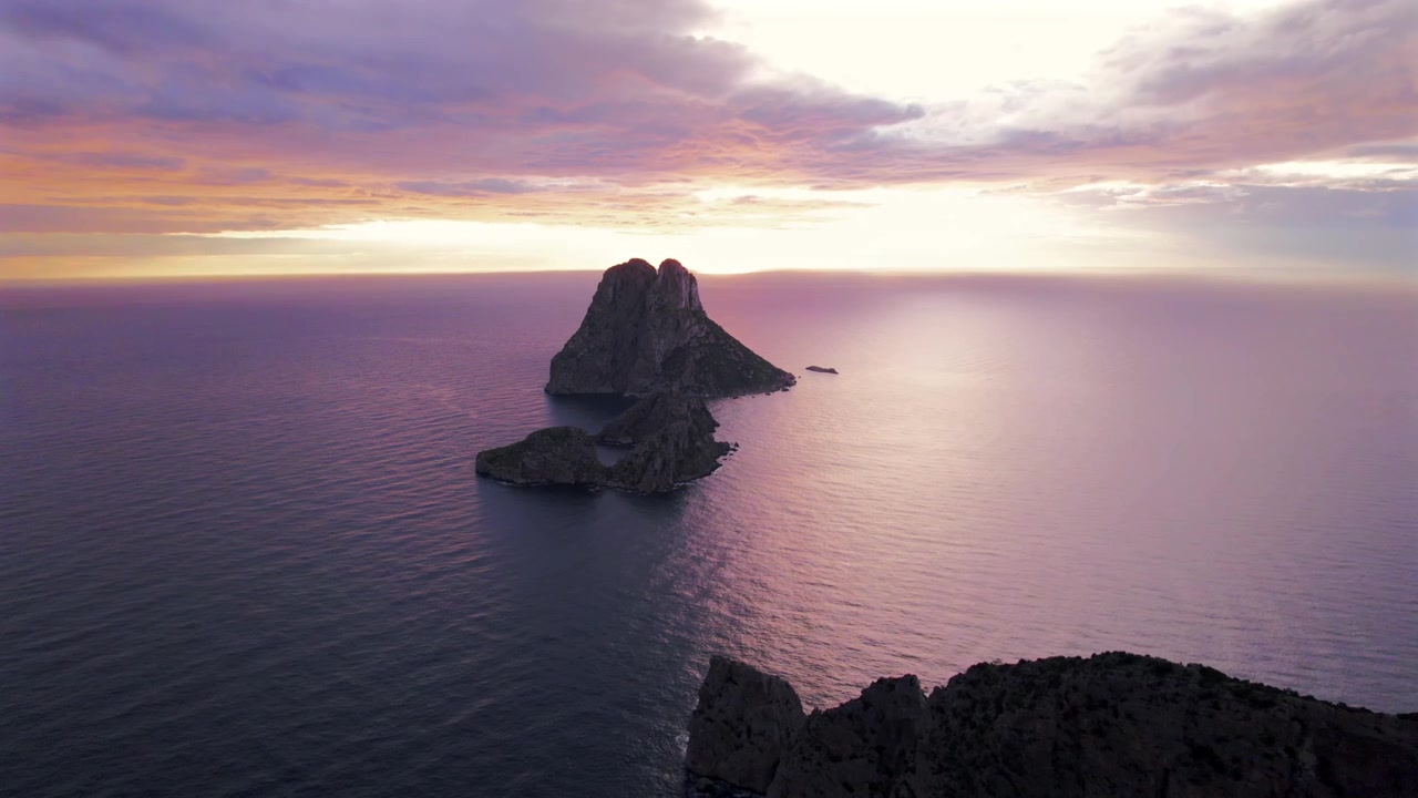 Ripresa aerea in 4K con drone di Es Vedrà al tramonto, Ibiza, Spagna. L'iconica isola rocciosa emerge dal Mar Mediterraneo mentre una calda luce dorata illumina la costa e le acque circostanti