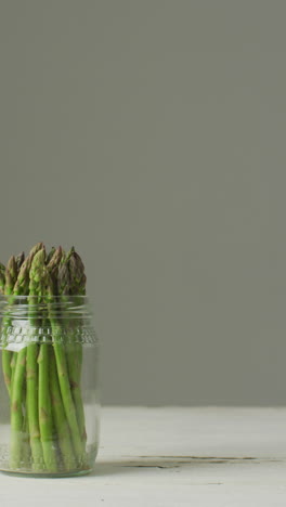 vertical video of fresh stalks of asparagus in glass jar on grey background