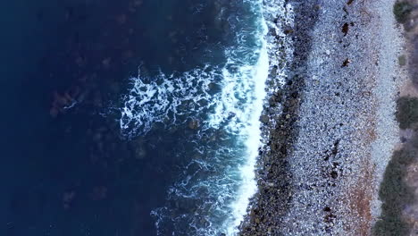 waves crashing against a picturesque rocky shoreline - tilt up aerial reveal