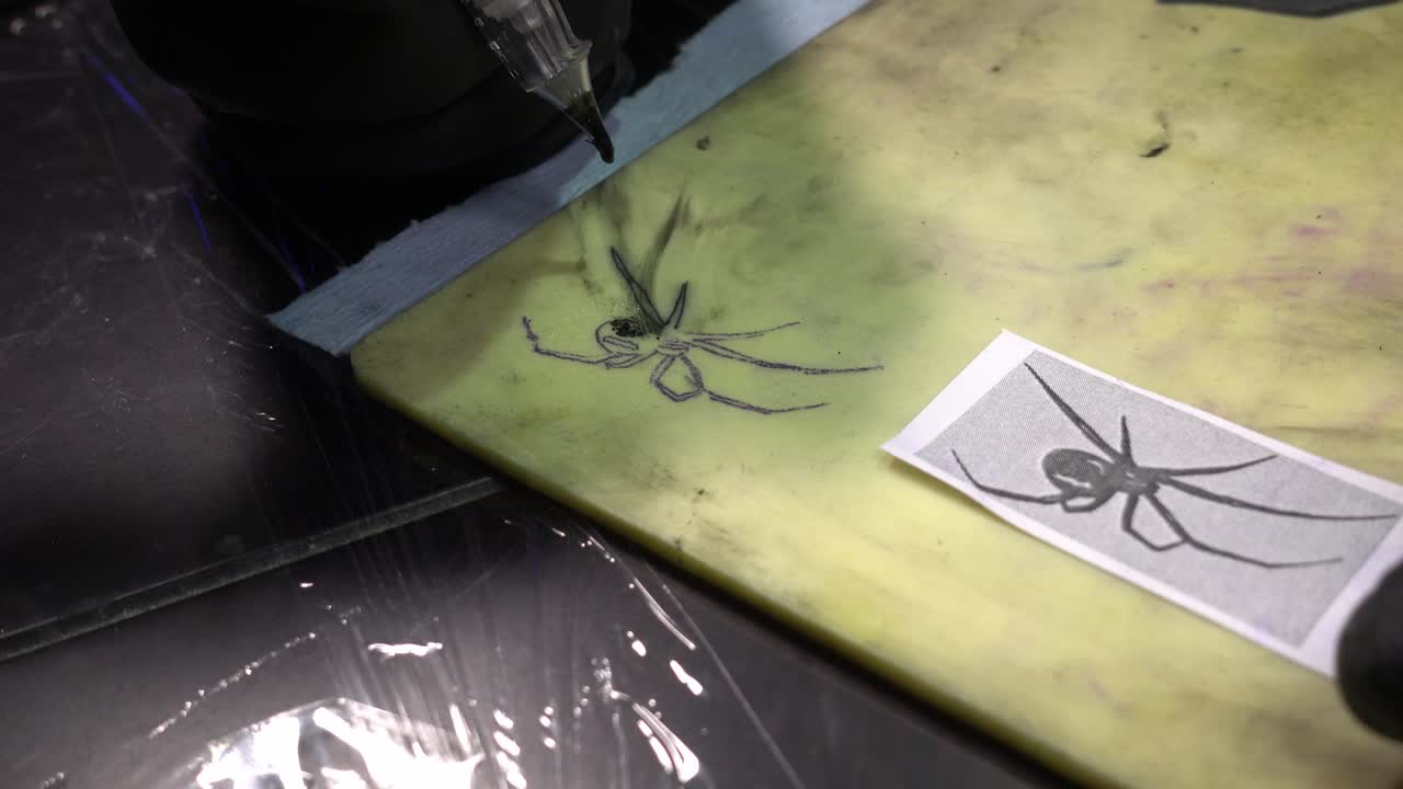 татуировщик рисует черного паука на синтетической коже