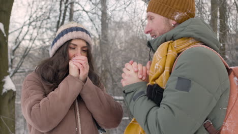 husband and wife in winter clothes warm their hands with their mouths in a snowy forest 1