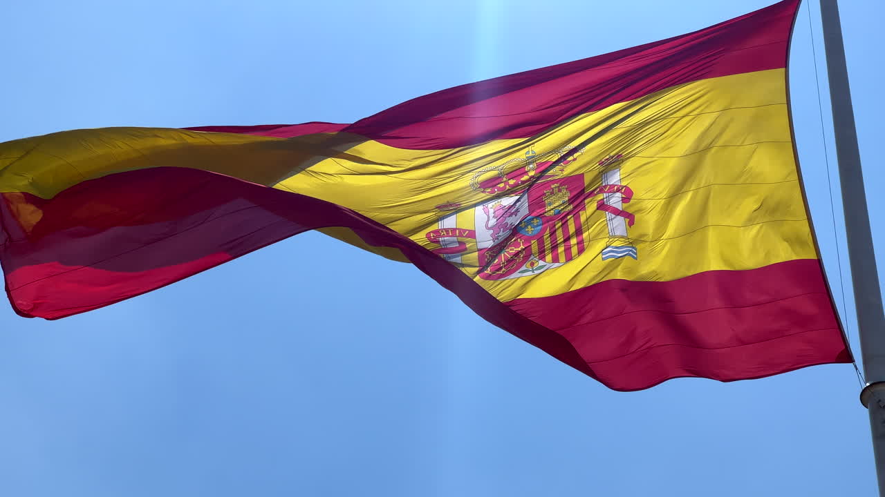 Grande e maestosa bandiera nazionale spagnola su un'asta che sventola con cielo blu a Madrid, Spagna, giornata di sole, bandiera nazionale spagnola, ripresa in 4K