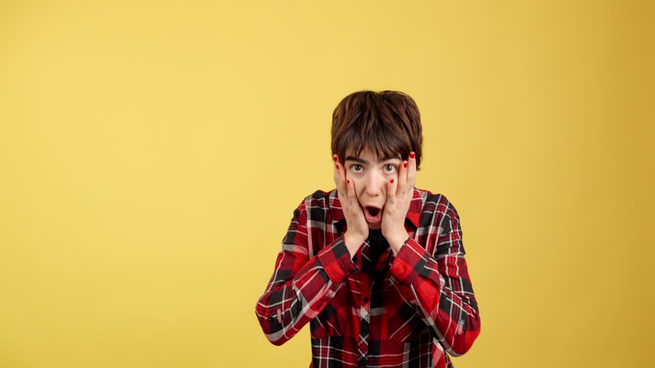 Shocked or Surprised Young Person in Plaid Shirt on Yellow Background