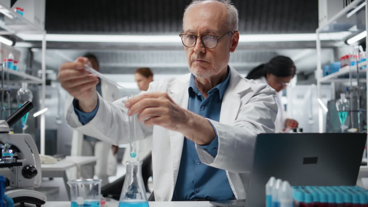 Elderly researcher inspecting blue liquid clarity in test tube, using laptop