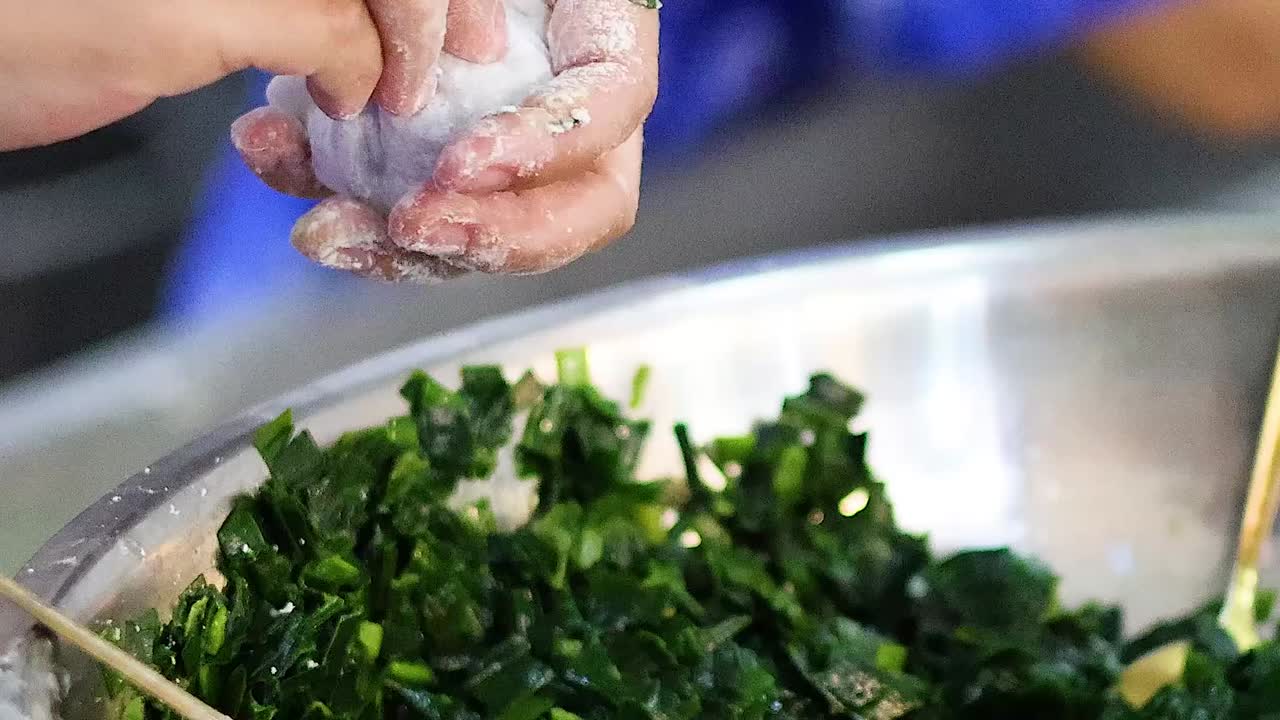 Hands skillfully shape dumplings with a leafy green filling, showcasing precise culinary techniques.