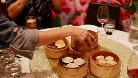 hands distribute bamboo steamers with dim sum at a round table. warm lighting creates a cozy dining atmosphere