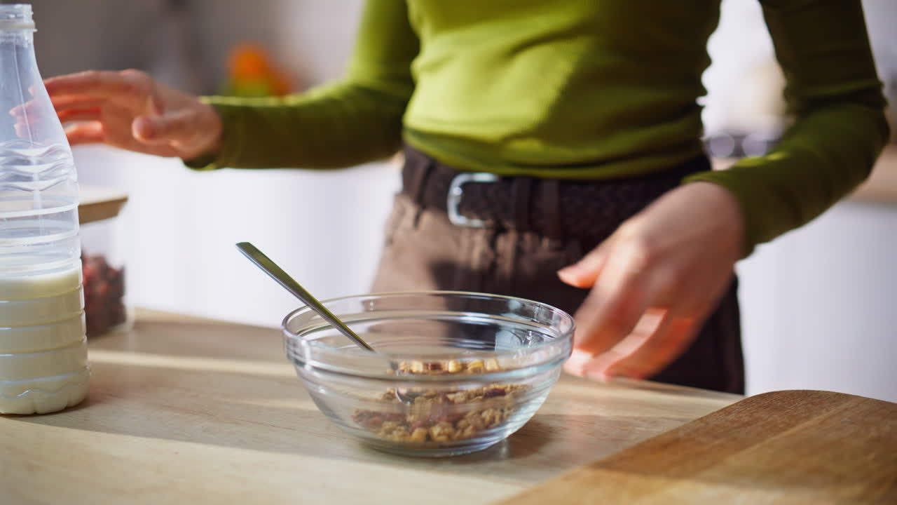 Primo piano di una donna bionda che annusa le bacche mentre prepara la granola fatta in casa in una cucina moderna.