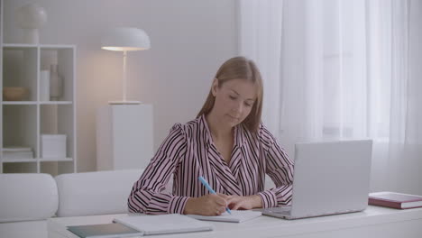 online learning session at home young woman is looking at display of laptop and writing in copybook distant education