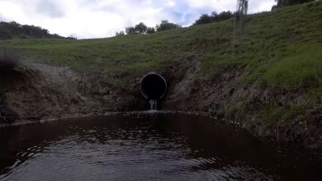 el dron comienza cerca de una alcantarilla y luego retrocede siguiendo el agua que escapa del arroyo