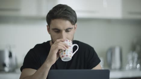 hombre serio bebiendo café trabajando en casa. hombre de negocios enfocado trabajando en una computadora portátil