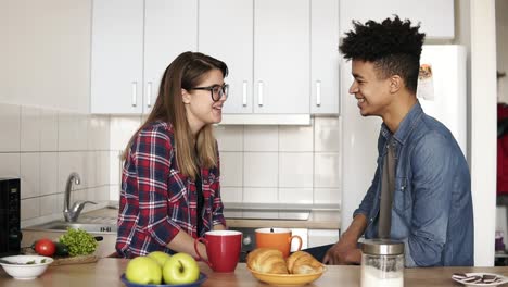Tender,-caring-mulatto-guy-tucks-his-happy-caucasian-girlfriend's-hair-behind-her-ear,-they're-having-interesting-conversation-in-the-kitchen.-Couple-goals,-enjoying-time-together.