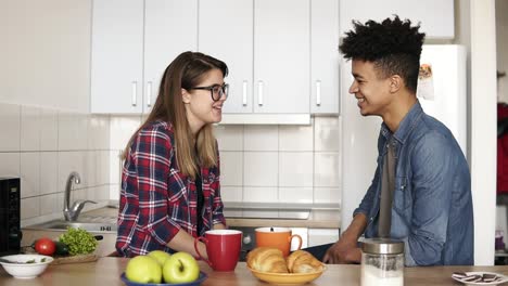 Un-Mulato-Tierno-Y-Cariñoso-Mete-El-Pelo-De-Su-Feliz-Novia-Caucásica-Detrás-De-La-Oreja,-Están-Teniendo-Una-Conversación-Interesante-En-La-Cocina.-Metas-De-Pareja,-Disfrutar-Del-Tiempo-Juntos.