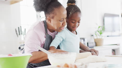 Happy-african-american-grandmother-and-granddaughter-baking-in-kitchen,-rolling-dough,-copy-space