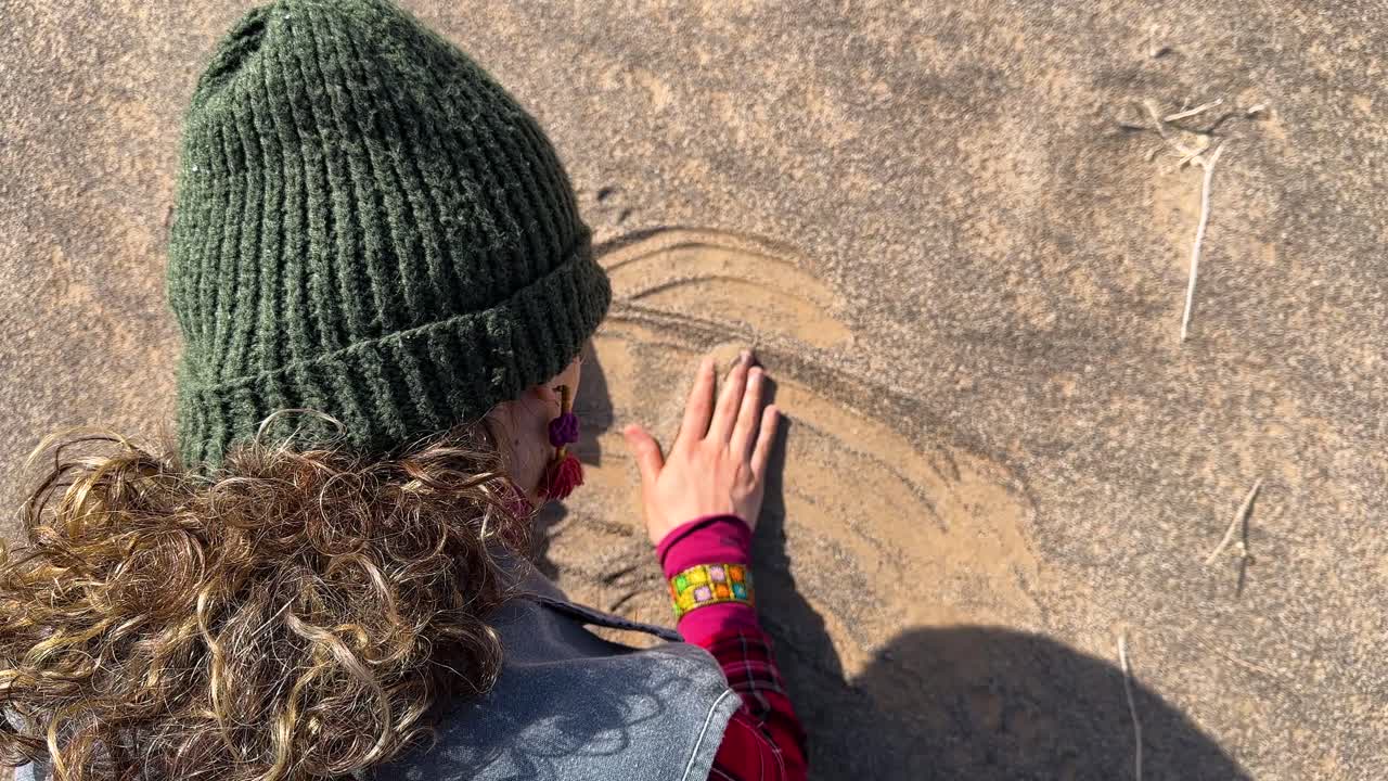 Iranian curly hair woman with red dress touch the golden sand desert in Saudi wonderful nature landscape close up dune fine sand pouring landscape of orange sky summer outdoors traveler journey