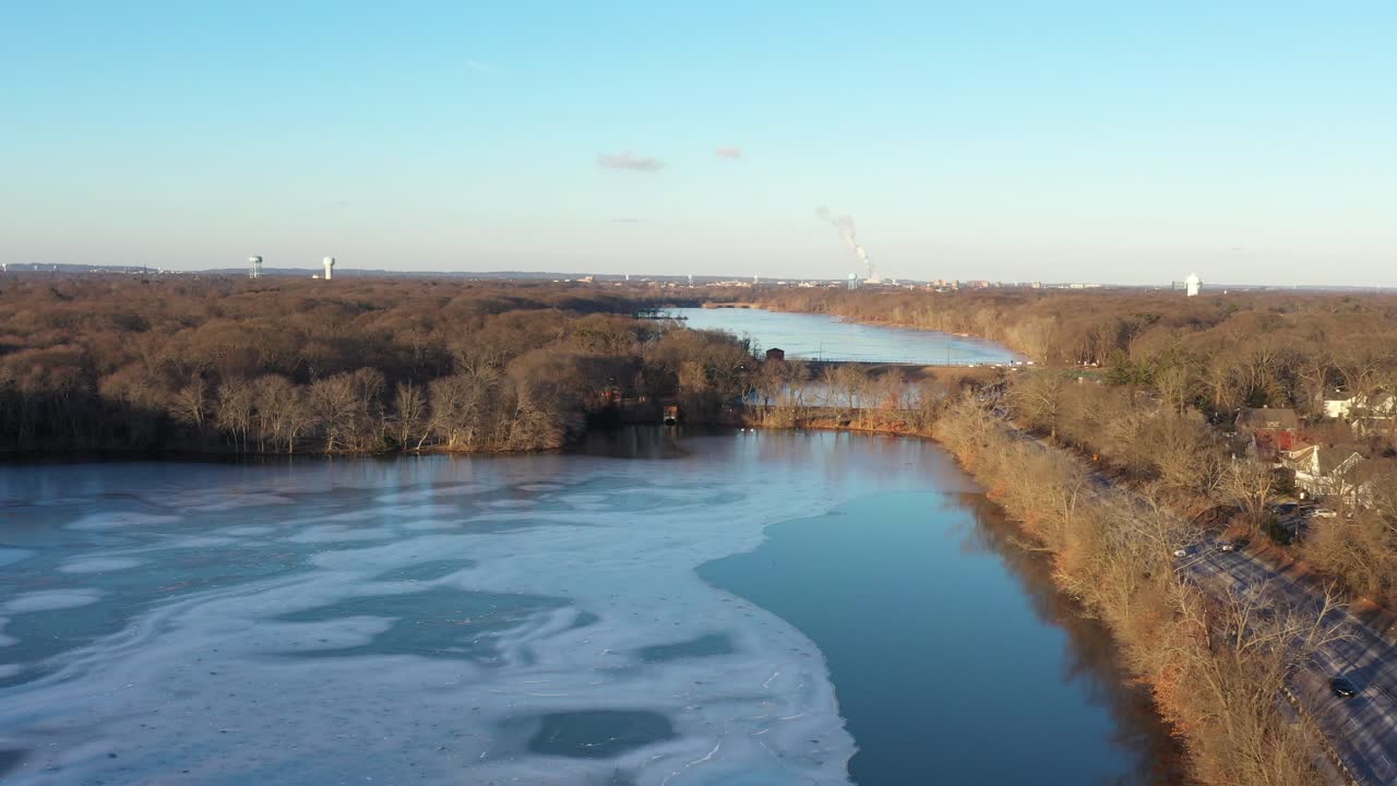 An aerial shot over frozen lakes on a sunny evening by a multilane boulevard with a few cars driving by