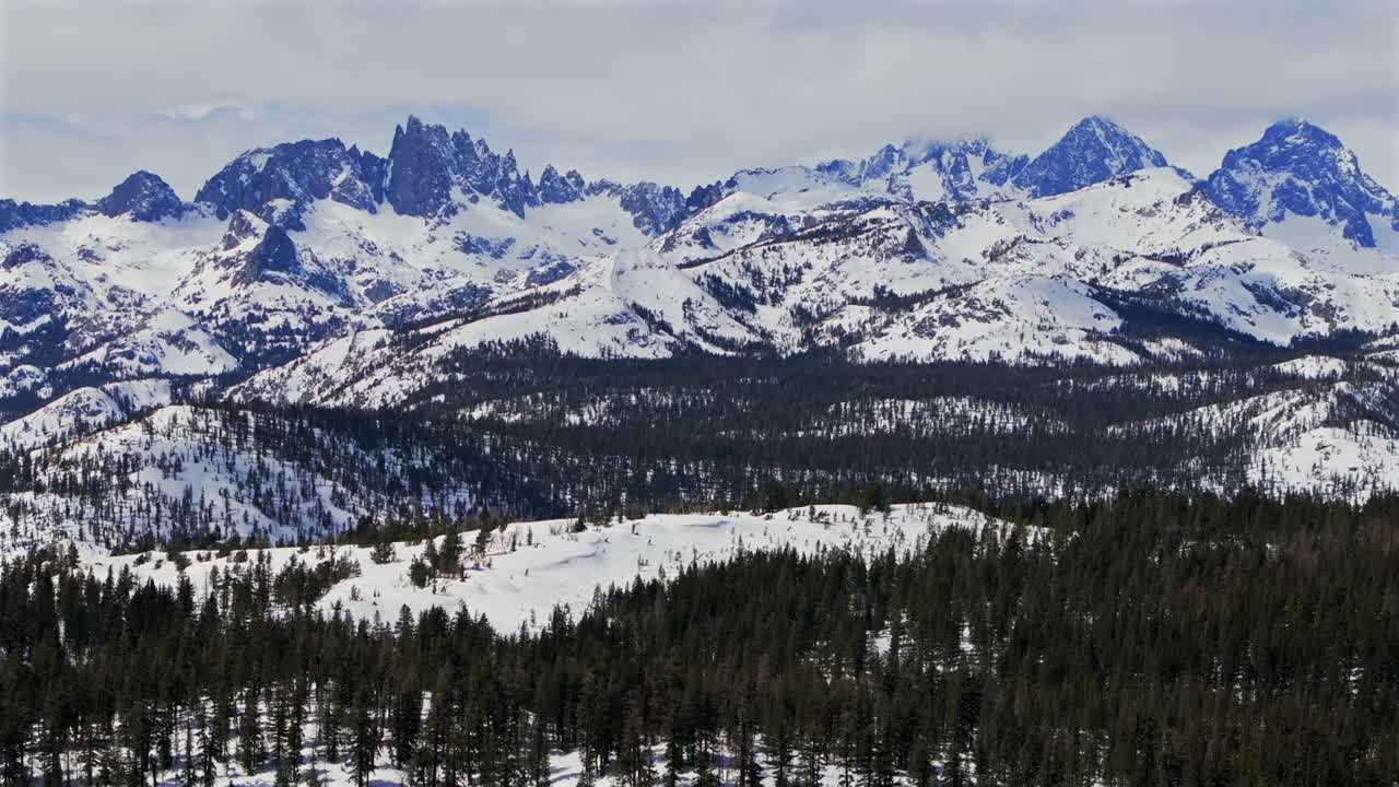 The stunning winter spring snowy jagged towering peaks of the Minarets Summit Mountains Mammoth Lakes California aerial drone sunny clouds daytime deep backcountry snow PCT vista point forward pan up
