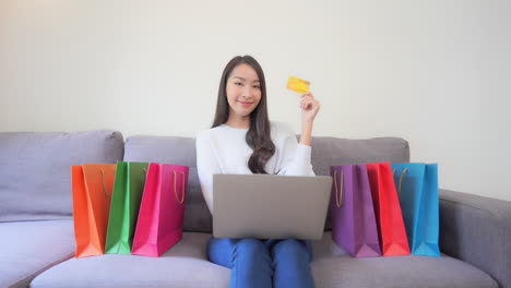 a young asian woman in her 30th surrounded with shopping bags show off her golden discount credit card with a happy and excited face expression