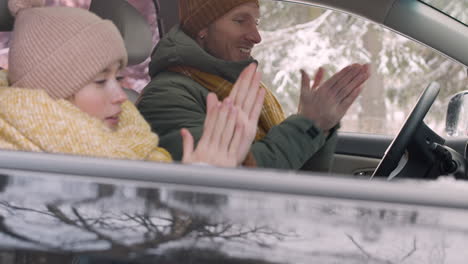 Side-View-Of-A-Girl-And-Her-Father-Sitting-In-The-Car-Warming-Their-Hands-With-Their-Mouths-And-Putting-Them-In-The-Air-Conditioner