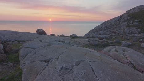 Una-Escultura-De-Equilibrio-De-Rocas-Construida-En-La-Cima-De-Una-Montaña,-Con-Vista-Al-Océano-En-Calma-Con-Una-Hermosa-Puesta-De-Sol-Rosa-Y-Un-Cielo-Despejado