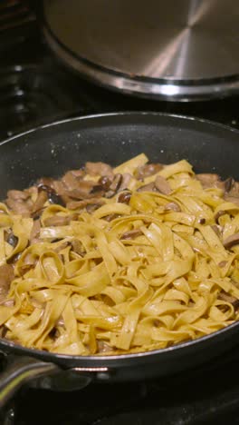 vertical video cooking shot of mushroom tagliatelle in hot frying pan with various fungi including champignon, shitake, nameko. home cooked cream sauce based pasta dish.
