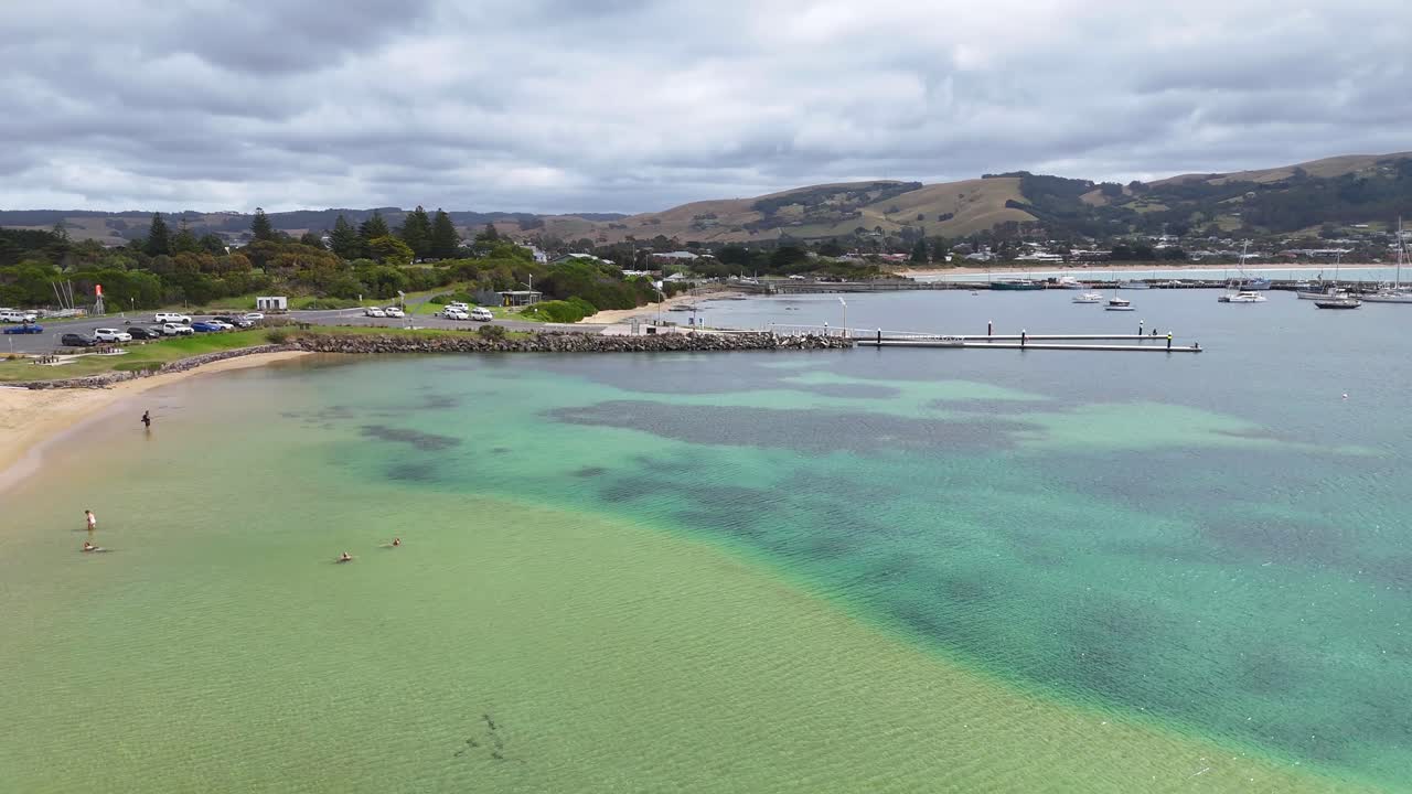 Drone footage captures Port Campbell's vibrant turquoise waters and rocky shoreline under cloudy skies, highlighting the coastal landscape's natural beauty